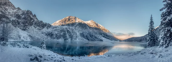 Wall murals Tatra Mountains Amazing beautiful scenic of Tatra mountains and Eye of the Sea lake, Poland. Bright sunrise above mountains in winter. Fir woods covered snow. The lake is not covered with ice.  