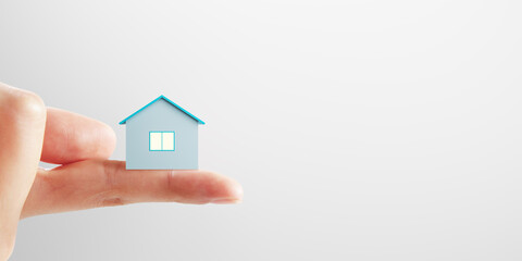 Fototapeta na wymiar Mortgage concept with small blue house layout on human finger on blank light background with place for advertising poster or your logo, mock up