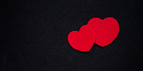 Two red hearts made of fabric on a black background.Romantic background for the ad. A red heart carved out of felt.