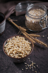 Bowl of cooked peeled barley grains porridge with ears of wheat on dark wooden background. Cooking Healthy and diet food concept.