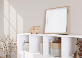 Fototapeta na wymiar Empty square picture frame standing on sideboard in modern child room. Frame mock up in contemporary style. Free, copy space for picture, poster. Toys, pampas grass. Close up view. 3D rendering.