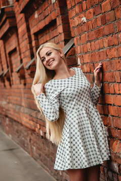 Portrait jewish young blonde woman model with long hair at brick wall background, smiling looking away. Pretty lady in white dress posing outdoors. Concept positive emotion, fashion. Copy text space