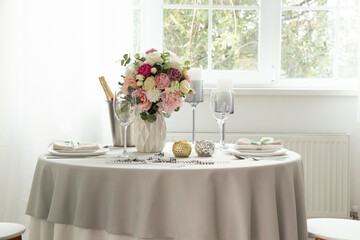 A festive table with serving dishes and a bucket of champagne in an apartment near a window with white walls