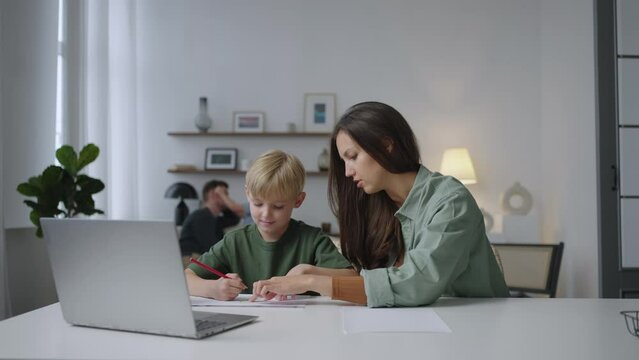 Woman with her child doing homework or studying sitting together at table in living room. Studying at home.