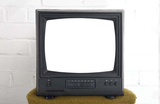 An old black vintage TV with a white screen against a brick wall in the 1980s, 1990s, 2000s.