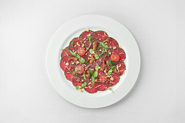 Veal carpaccio with spices and oil on a white plate on a white tablecloth. Close-up, selective focus