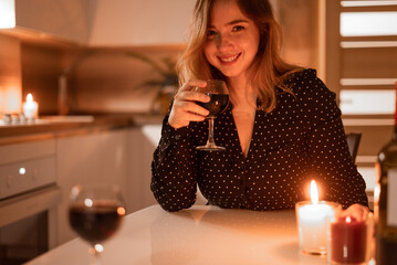 Beautiful woman in a black dress having a glass of wine, on date with partner. Indoors lifestyle portrait with candles.