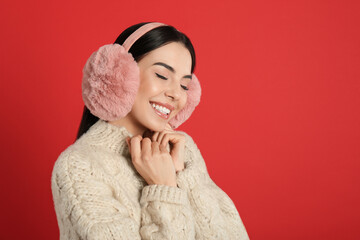 Beautiful young woman wearing earmuffs on red background. Space for text
