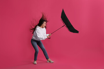 Emotional woman with umbrella caught in gust of wind on pink background © New Africa