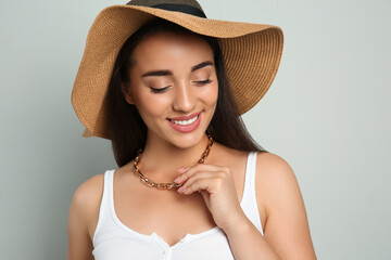 Beautiful young woman wearing straw hat on light grey background. Stylish headdress