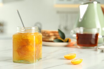 Delicious kumquat jam in jar on white marble table