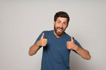 Handsome bearded man showing thumbs up on light grey background - obrazy, fototapety, plakaty
