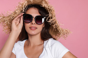 Beautiful woman with stylish straw hat and sunglasses on pink background