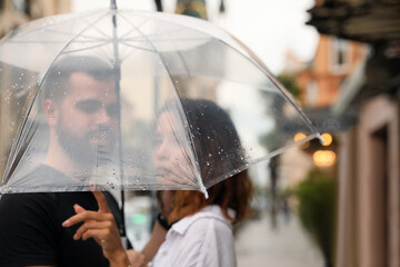 Young couple with umbrella enjoying time together under rain on city street