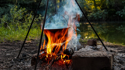Relaxing and cooking over a campfire in the woods on a fishing trip. Summer mood, outdoor food in the forest. Cooking shish kebab and fish soup on a campfire at a picnic outside the city.