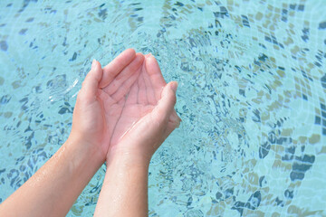 Girl holding water in hands above pool, closeup. Space for text
