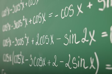 Many different math formulas written on green chalkboard, closeup