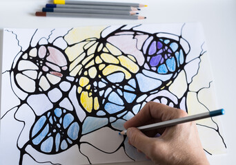 Abstract neurographic drawing. A woman draws a neurographic drawing on paper with color pencils....