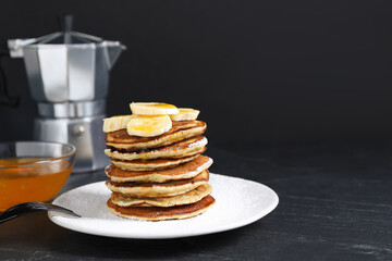 Plate of banana pancakes with honey and powdered sugar served on black table. Space for text
