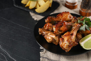 Plate with delicious fried chicken wings on black table, space for text