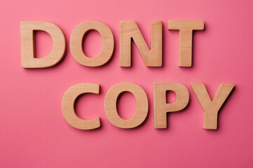 Words Don't Copy made of wooden letters on dark pink background, flat lay. Plagiarism concept