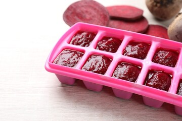 Beet puree in ice cube tray on white wooden table, closeup. Ready for freezing