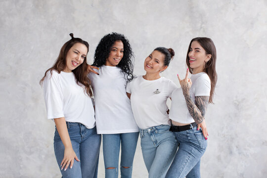 Group Young Women Stand Isolated Against Wall Background, Looking At Camera, Fun And Show Cool Gesture. Portrait Of Female Multi Ethnic Models Smile, Wear White T-shirts And Jeans