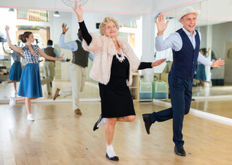 Man and elderly woman performing jazz dance in dancing room