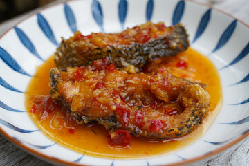 Fried fish with chilli in a ceramic plate on an old wooden floor. The taste is sour, sweet and slightly spicy.