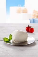mozzarella with tomato and basil leaf on round silver plate, resting on white wooden table