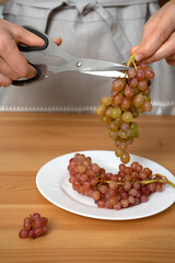 woman cuts a bunch of quiche-mish grapes into portioned dishes with kitchen scissors. Soft focus. Goods for the home, diet food based on vegetable raw materials. Healthy food