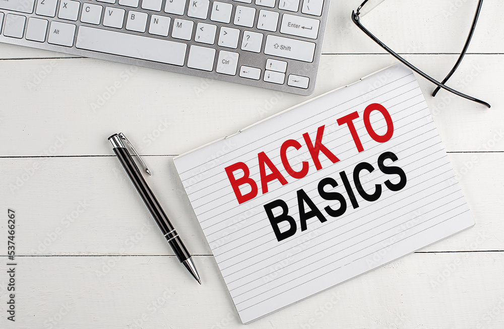 Poster back to basics text on notebook with keyboard , pen glasses on white wooden background