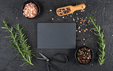 Empty black slate board with rosemary, salt and pepper on black background, copy space