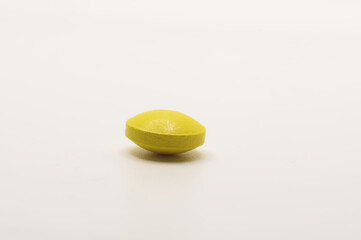 Żółta tabletka witaminy C na białym tle.