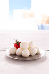 morsels of mozzarella with tomato on round silver plate resting on white wooden table