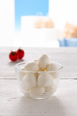 morsels of mozzarella in a glass bowl with tomatoes resting on a white wooden table