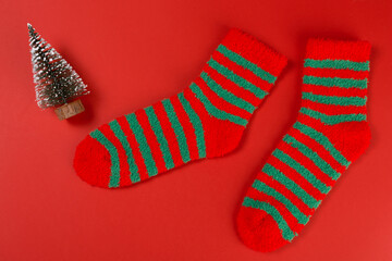 Two green striped Christmas socks, as if walking, next to the Christmas tree, concept, on a red background