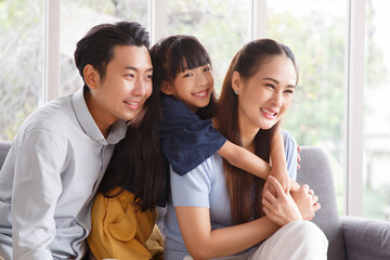 Fototapeta na wymiar Portrait of a happy young family. Mom, dad and daughter look at the camera and smile. The faces of Asian parents and their child in living room.