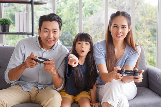 Portrait of asian nice cute lovely attractive cheerful positive funny people mom dad and daughter holding joystick attending contest competition sitting on sofa free time in living room.