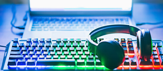 Pro gaming illuminated desk, headset, keyboard, computer neon lights. Cyber sport equipment laying on desktop, ready for online video gaming.Dark shot.Banner,advertisement. © ARVD73