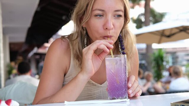 Woman dipping a straw into lemonade. Girl drinking a cold non-alcoholic cocktail in a cafe.