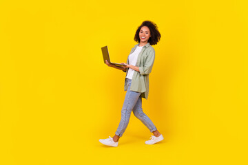 Full size profile photo of hr young brunette lady go hold laptop wear shirt jeans sneakers isolated on yellow background