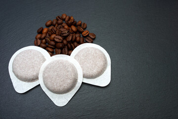 Coffee pods, coffee beans on a black slate board.