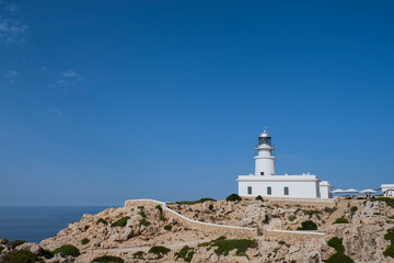 Fototapeta na wymiar white lighthouse on top of a rocky cliff with white walls surrounding it and the sea in the background, Cavalleria cape lighthouse, Fornells, Menorca Spain