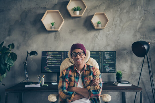 Photo of clever confident programmer wear spectacles hat arms crossed coding indoors workplace workshop home