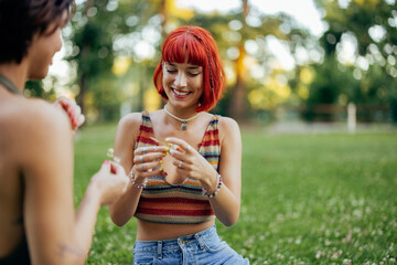 Focus on the smiling red haired girl, making a necklace of flowers.