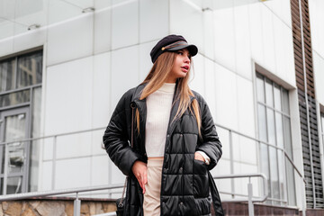 Elegant young woman in black coat and beret standing near office building looking away outdoor