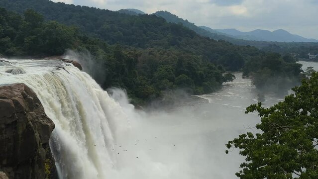 beautiful and majestic waterfalls at the center of a deep green forest surrounded by hills and mountains 