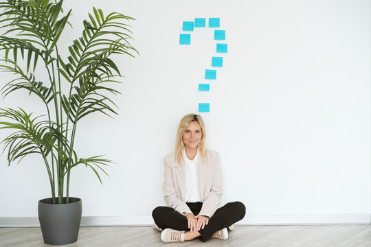 Businesswoman Sitting On The Floor In Office With Question Mark Above Her