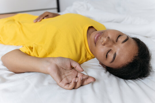 Exhausted Woman In Yellow T-shirt Sleeping On Bed At Home